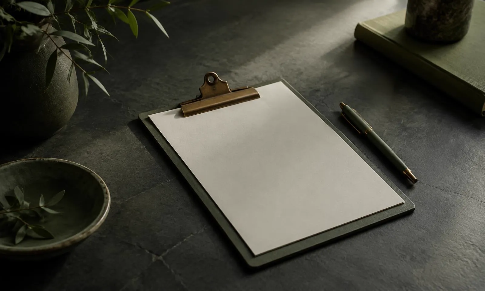 A blank clipboard and pen on a dark desk