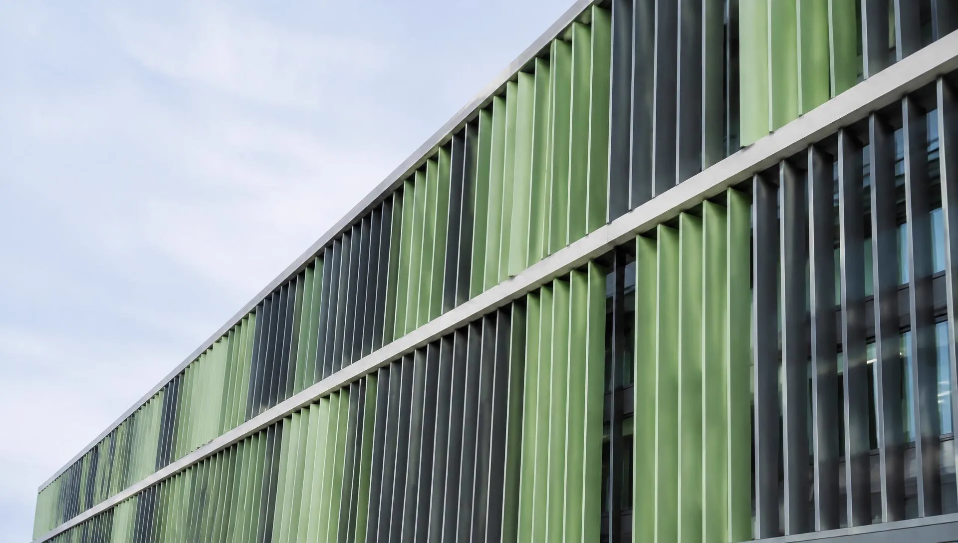 Sage and slate louvers on a modern building against a pale sky